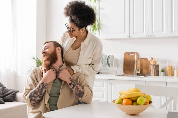 Femme afro-américaine positive étreignant petit ami tatoué dans la cuisine — Photo de stock