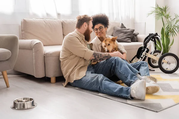 Tattooed man talking to african american girlfriend near wheelchair in living room — Stock Photo