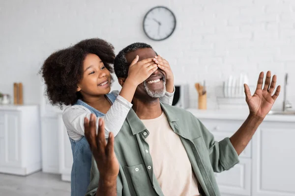 Menina americana africana feliz com cabelos cacheados cobrindo os olhos do avô sorridente em casa — Fotografia de Stock