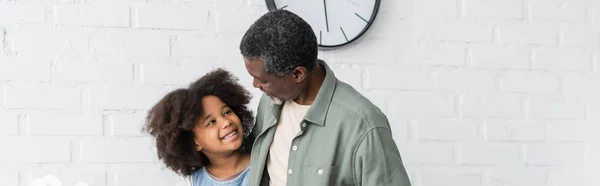 Bärtiger afrikanisch-amerikanischer Großvater schaut lächelnde Enkelin in Küche an, Banner — Stockfoto