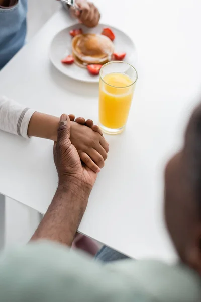 Vista superior de la chica afroamericana cogida de la mano con el abuelo durante el desayuno - foto de stock