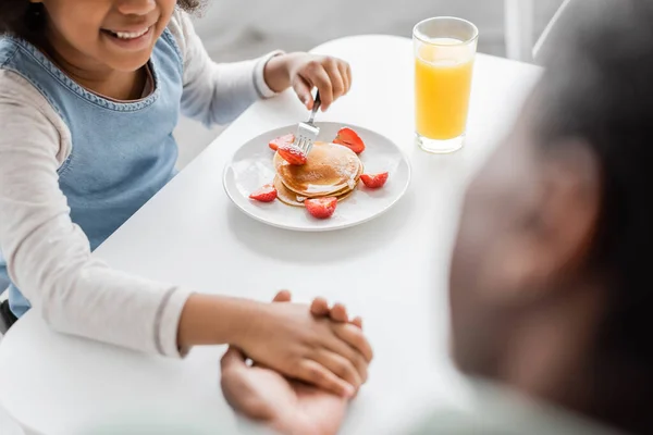 Високий кут зору щасливої афроамериканської дівчини, що тримає руки з дідом під час сніданку — стокове фото