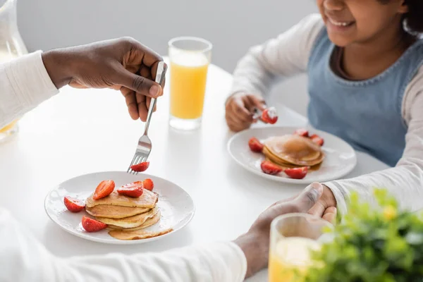 Vista recortada de la alegre chica afroamericana cogida de la mano con el padre durante el desayuno - foto de stock