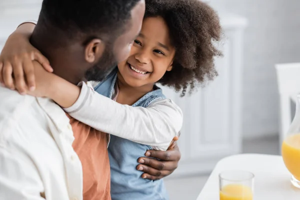 Rizado africano americano chica sonriendo mientras abrazando padre en casa - foto de stock