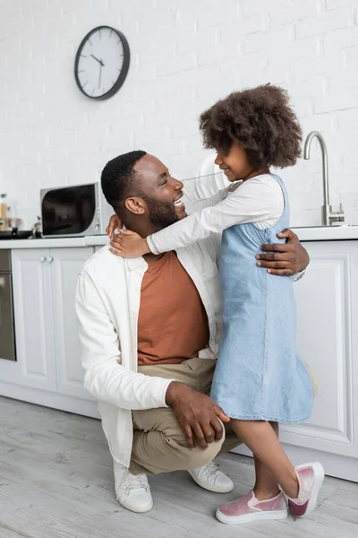 Freudige afrikanisch-amerikanische Mädchen im Jeanskleid umarmt glücklichen Vater in der Küche — Stockfoto