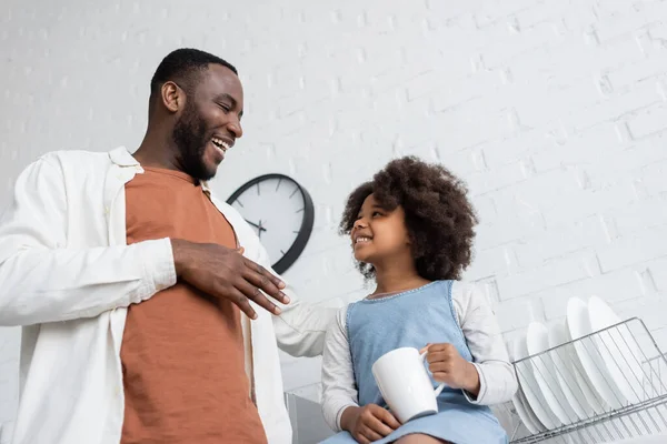 Blick aus dem niedrigen Winkel auf fröhliche afrikanisch-amerikanische Kinder, die eine Tasse Tee in der Hand halten und den glücklichen Vater betrachten — Stockfoto