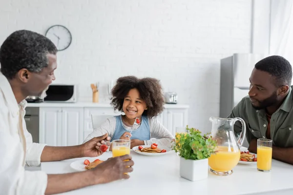 Garoto americano africano feliz olhando para o vovô enquanto toma café da manhã em família — Fotografia de Stock