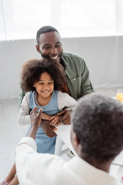 Щасливий афроамериканський чоловік обіймає кучеряву дочку і дивиться на батька на розмитому фоні — стокове фото