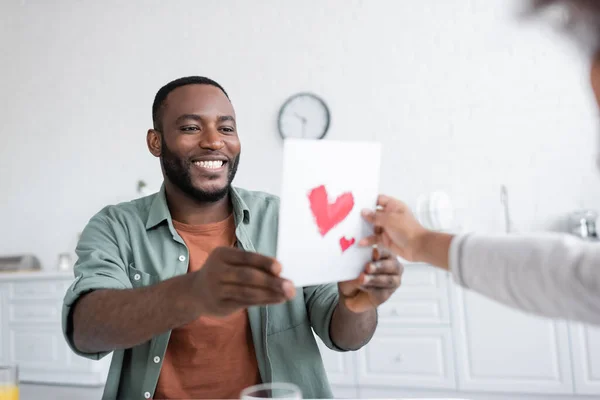 Afrikanerin überreicht Glückwunschkarte mit gezeichneten Herzen an glücklichen Papa am Vatertag — Stockfoto
