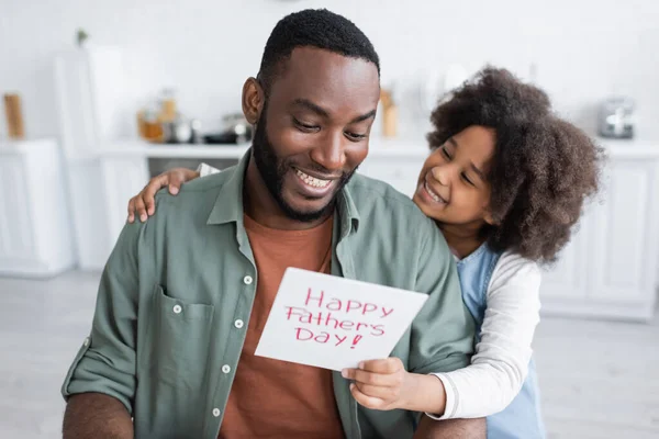 Menina afro-americana dando cartão de saudação com feliz dia pais lettering ao pai alegre — Fotografia de Stock