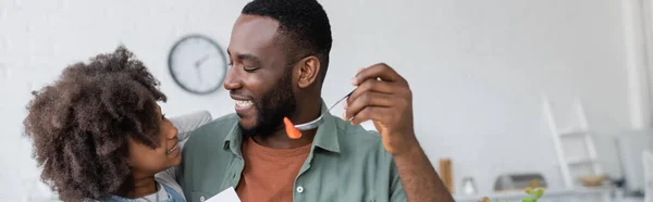 Homme afro-américain gai tenant fourchette avec fraise fraîche et regardant fille heureuse, bannière — Photo de stock