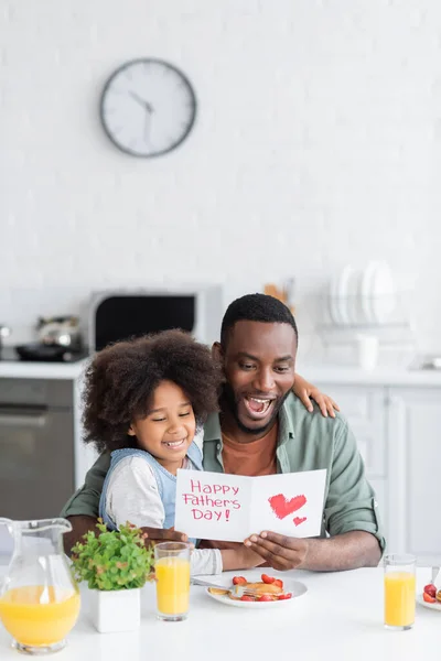 Здивований афроамериканський чоловік читає вітальні листівки з щасливими батьками день, пропускаючи біля милої дочки — стокове фото