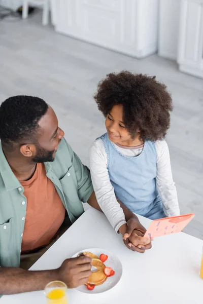 Top view of curly african american girl holding greeting card near cheerful dad on fathers day — Stock Photo