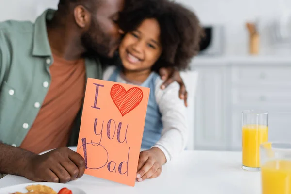 Afrikanisch-amerikanischer Mann küsst Tochter und hält Grußkarte mit ich liebe dich Papa-Schriftzug am Vatertag — Stockfoto
