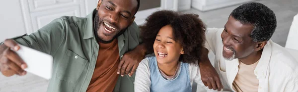 Allegro uomo afroamericano che prende selfie su smartphone con figlia e padre felici, banner — Foto stock
