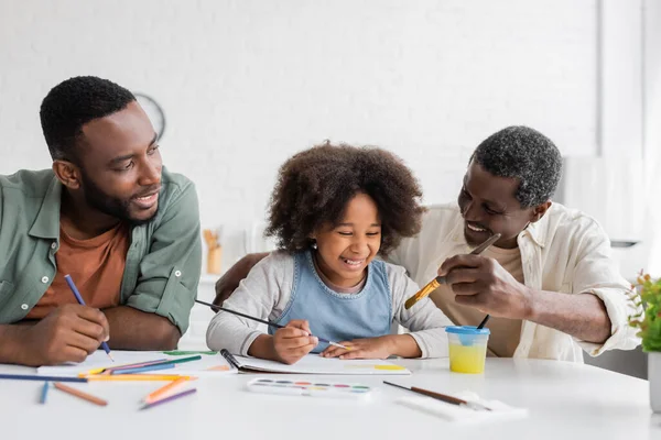 Alegres padres afroamericanos pintando con niños en casa - foto de stock
