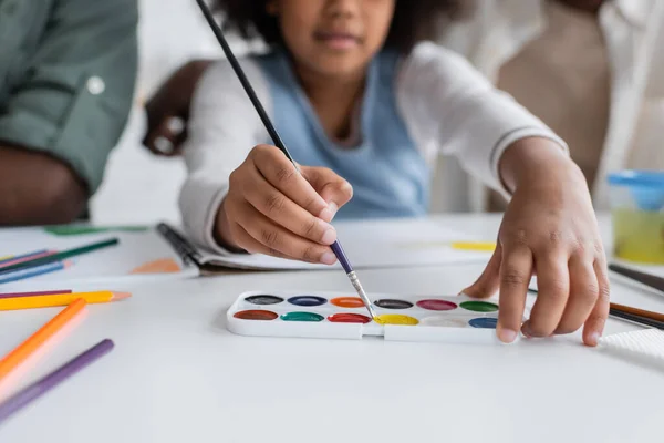 Cropped view of blurred african american girl painting with watercolor near parents at home — Stock Photo