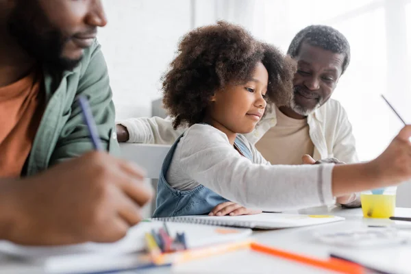 African american child painting near blurred father and grandpa at home — Stock Photo