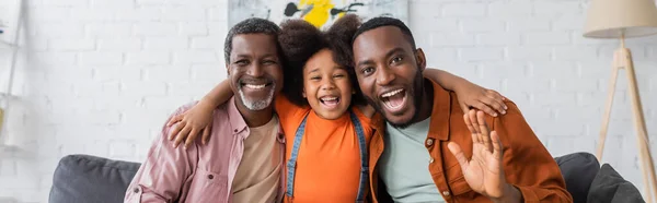 Ragazza afroamericana spensierata che abbraccia nonno e papà in soggiorno, banner — Foto stock