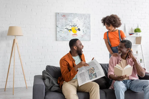 Fröhliches afrikanisch-amerikanisches Kind und Großeltern schauen Mann mit Zeitung zu Hause auf Couch an — Stockfoto
