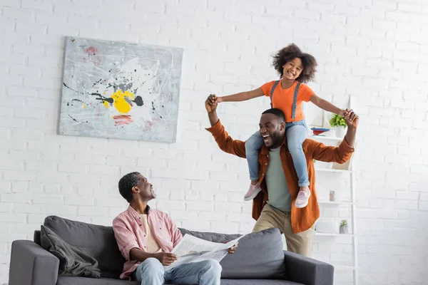 Grand-parent afro-américain tenant journal près de fils et petite-fille s'amuser à la maison — Photo de stock