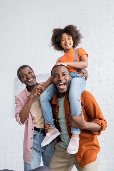 Alegre africano americano hombre tener divertido con hija y maduro padre en casa - foto de stock