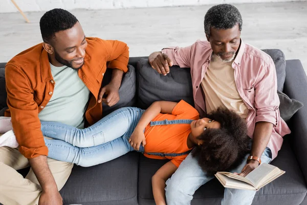 High angle view of african american girl lying near father and granddad with book at home — Stock Photo