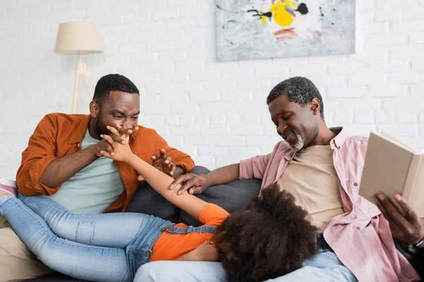 Cheerful african american parents with book playing with kid at home — Stock Photo