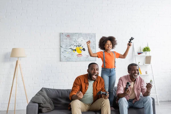 KYIV, UCRANIA - 17 de julio de 2021: Emocionada familia afroamericana jugando videojuegos en la sala de estar - foto de stock