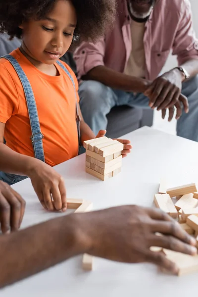 Criança afro-americana jogando jogo de blocos de madeira com pai desfocado perto do avô em casa — Fotografia de Stock