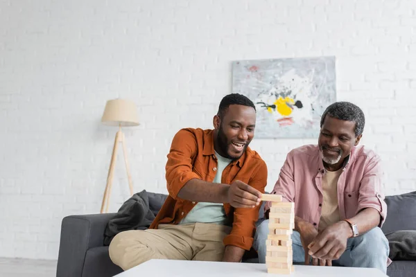 Fröhlicher afrikanisch-amerikanischer Mann spielt Holzklötzchen-Spiel mit reifem Vater im Wohnzimmer — Stockfoto