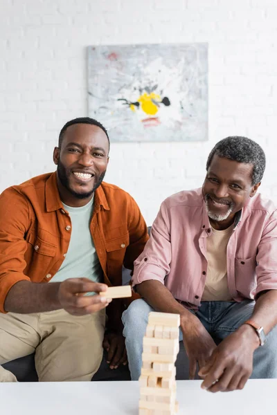 Cheerful african american father and son looking at camera near wood blocks game at home — Stock Photo