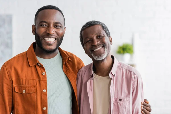 Positiver afrikanisch-amerikanischer Mann umarmt Vater und schaut zu Hause in die Kamera — Stockfoto