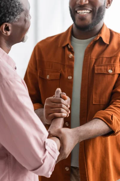 Smiling african american man holding hand of mature father at home — Stock Photo