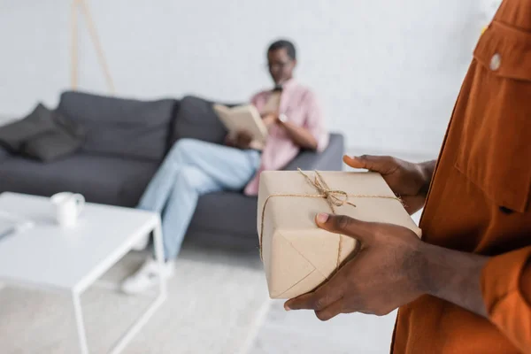 African american man holding gift box during father day celebration near blurred dad  at home — Stock Photo