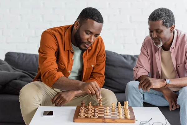 Africano americano homem jogando xadrez com pai maduro na sala de estar — Fotografia de Stock