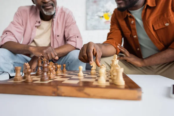 Vista recortada del hombre afroamericano jugando ajedrez con papá de mediana edad en casa - foto de stock