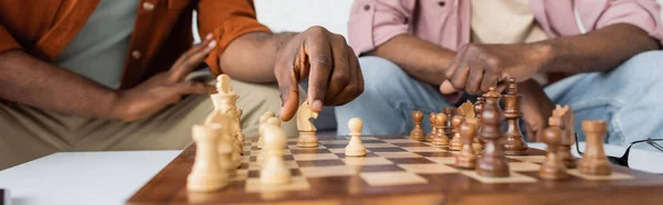 Vue recadrée d'un homme afro-américain jouant aux échecs avec un parent flou à la maison, bannière — Photo de stock