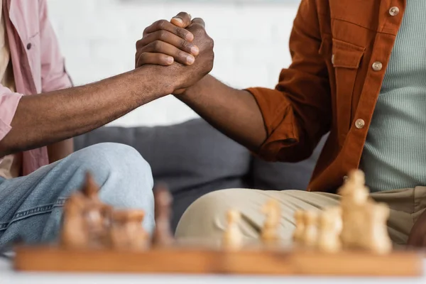 Розбитий погляд на афроамериканського чоловіка і сина, який тримається за руки біля розмитої шахової дошки вдома. — стокове фото