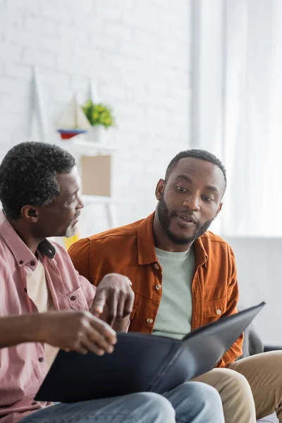 Mature african american man pointing at photo album near son at home — Stock Photo