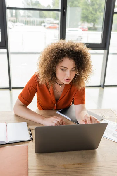 Hochwinkel-Ansicht der lockigen Geschäftsfrau mit Laptop in der Nähe leeres Notizbuch auf dem Schreibtisch — Stockfoto