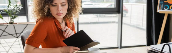 Concentrated businesswoman holding notebook and pen near cup of tea in office, banner — Stock Photo