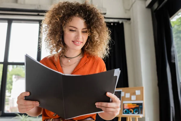 Low angle view of happy businesswoman with curly hair looking at folder in office — Stock Photo