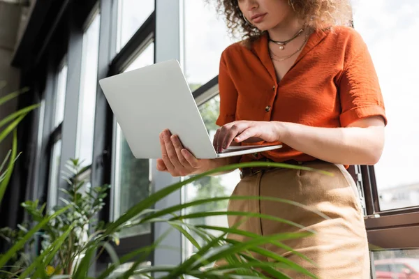 Cropped view of young businesswoman using laptop next to green plants in modern office — Stock Photo