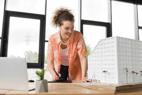 Cheerful designer looking at architecture model while using graphic tablet in office — Stock Photo