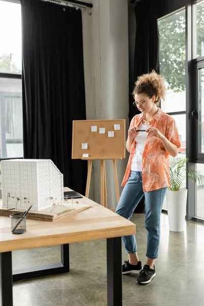 Designer de arquitetura feliz segurando stylus e olhando para o modelo de casa residencial no escritório — Fotografia de Stock