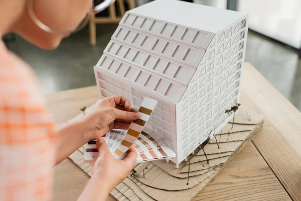 Cropped view of architectural designer holding color palette near residential house model in office — Stock Photo