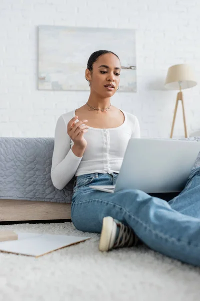 Pretty african american woman in jeans watching webinar on laptop — Stock Photo