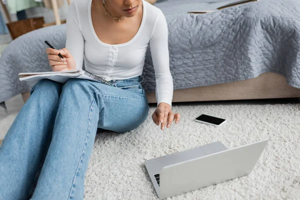 Vista cortada da mulher americana africana em jeans tomar notas enquanto assiste palestra on-line no laptop — Fotografia de Stock