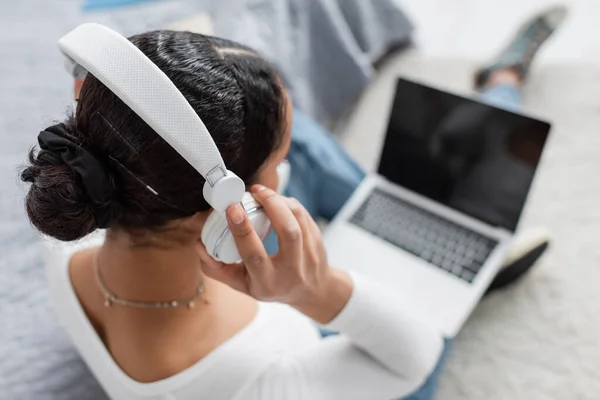 Ansicht von afrikanisch-amerikanischer Studentin mit drahtlosen Kopfhörern, während sie Podcast hört und Laptop benutzt — Stockfoto